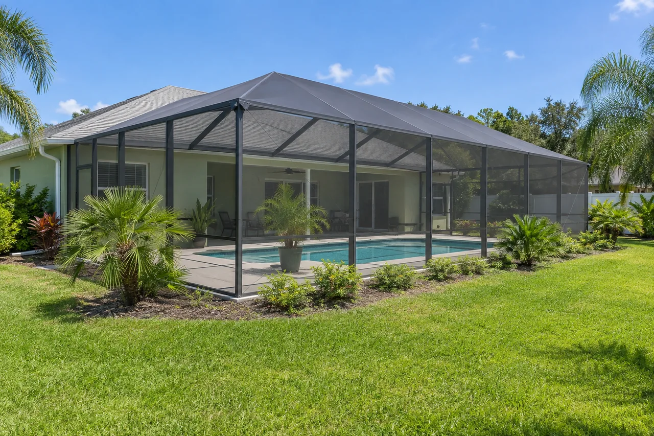 Dark screen enclosure behind a light green home with a spacious grassy yard