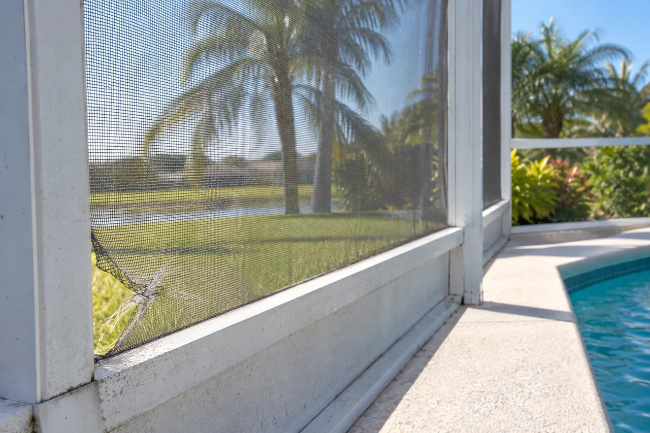 Frayed insect screen mesh at the corner of a sunlit white enclosure panel